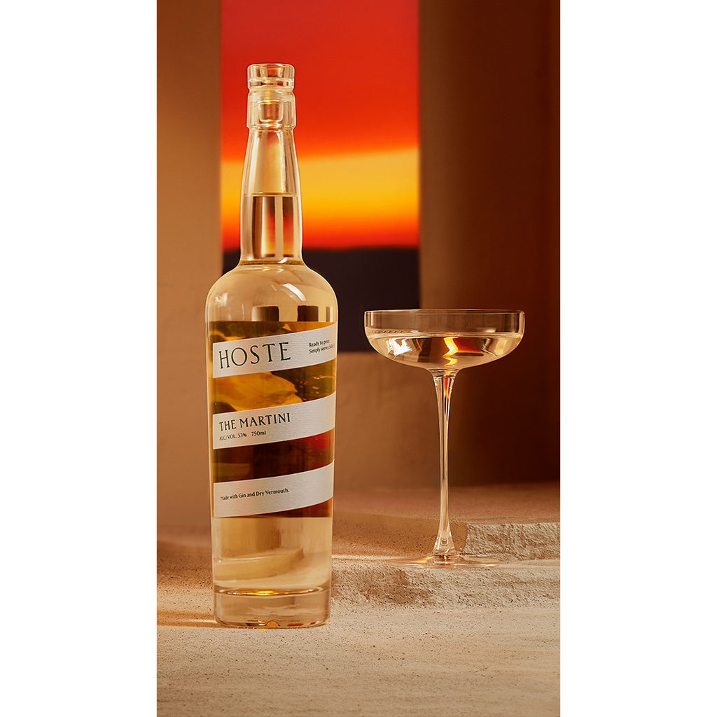 Bottle of Hoste The Martini on a table next to martini glass.