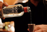 Bottle of Good Vodka being poured into a shot glass with a blurred background