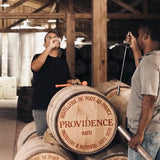 Two men tasting from barrels in a distillery with 'Providence' branding.