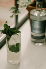 Clear glass with a mint leaf garnish on a surface with a bottle in the background