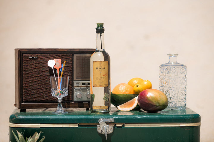 Bottle of alcohol on a green cooler with fruit and a vintage radio in the background