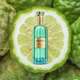 Bottle of Italicus Rosolio di Bergamotto Liqueur over backdrop image of a sliced piece of green fruit.