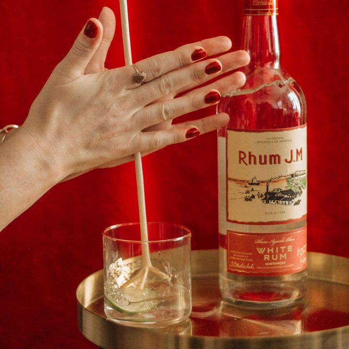 Person pouring white rum into a glass with a Rhum J.M bottle in the background.