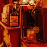 Bottle of rum and a cocktail with a lime wedge on a wooden shelf.