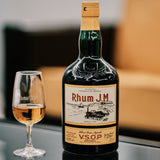 Bottle of Rhum J.M VSOP with a glass of rum on a reflective surface.