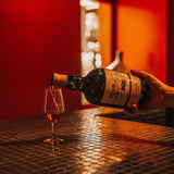 Person pouring rum into a glass on a bar counter with a red wall in the background