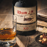 Bottle of Rhum J.M. rum with a glass and snacks on a wooden surface