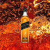 Bottle of Johnnie Walker Black Label over backdrop of orange liquid upclose. 