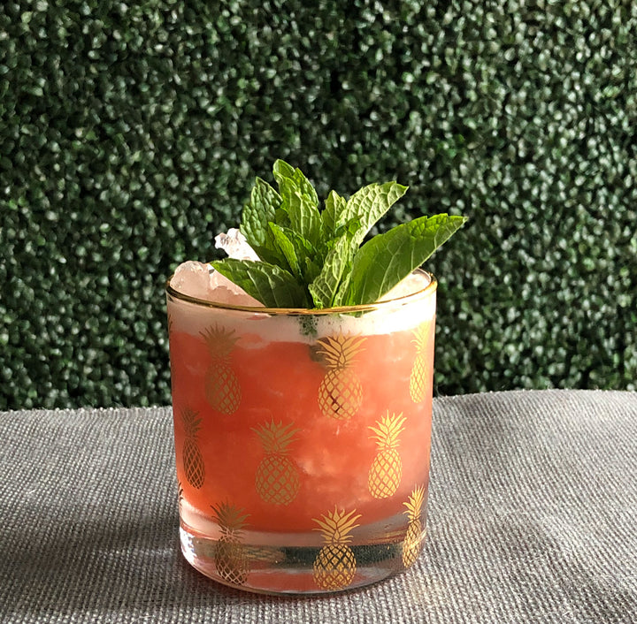 Cocktail in a glass with pineapple pattern against a green textured background