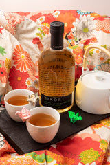 Bottle of Kikori with two cups of tea on a decorative tablecloth.