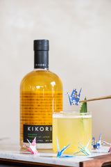 Bottle of Kikori whiskey with a glass of yellow liquid on a marble surface.