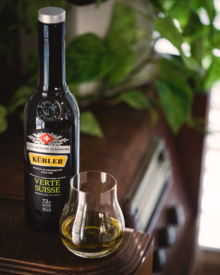 Kübler bottle of Verte Suisse liqueur with a glass on a wooden surface.