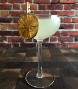 Cocktail in a glass with a lime garnish against a brick wall background