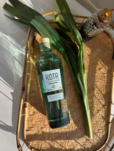 Kota bottle of gin on a woven tray with green leaves