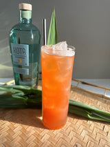 Cocktail with ice and a bottle of KOTA Liqueur on a woven surface.