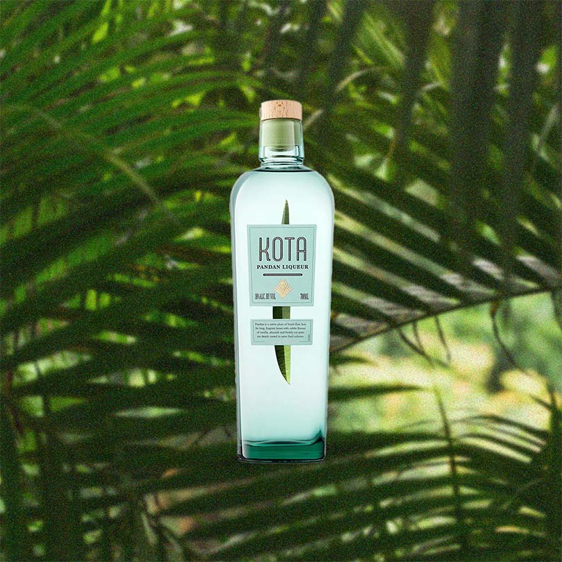 A bottle of Kota Pandan Liqueur over backdrop of green plant leaves.