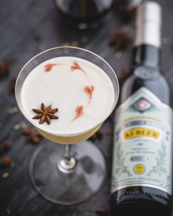 Cocktail with star anise garnish next to a bottle on a dark surface