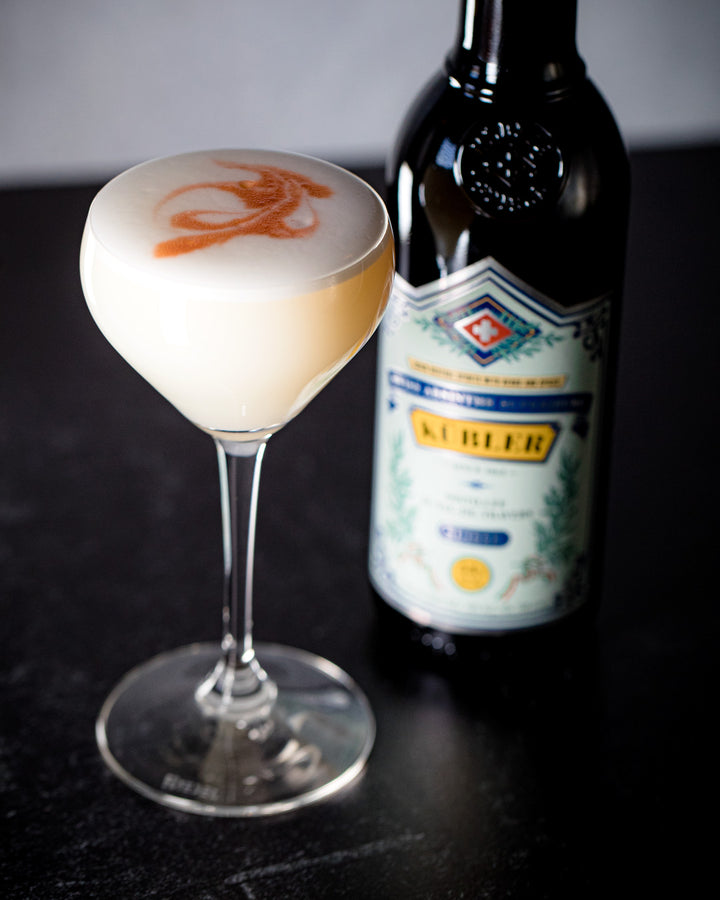 Cocktail in a glass with a bottle of K�bler in the background
