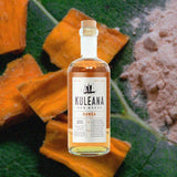 Kuleana Nanea bottle against a backdrop of dried mango, terracotta stone, and a large rich, green leaf.