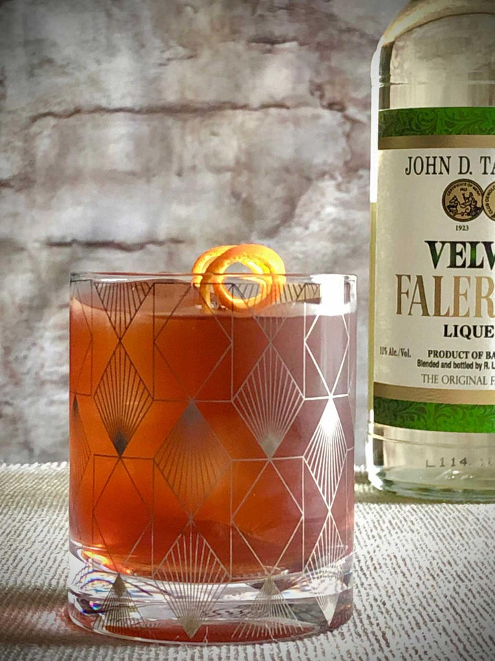Cocktail in a glass with geometric design next to a bottle of John D. T. Velvety Faleri Liqueur.