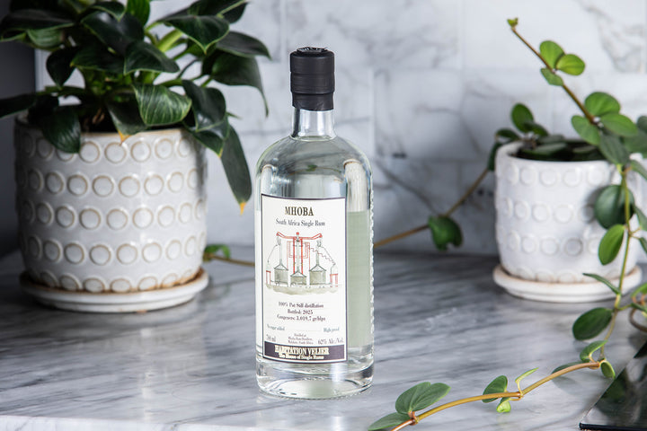 Bottle of Habitation Velier Mhoba Rum on a marble surface with plants in the background.