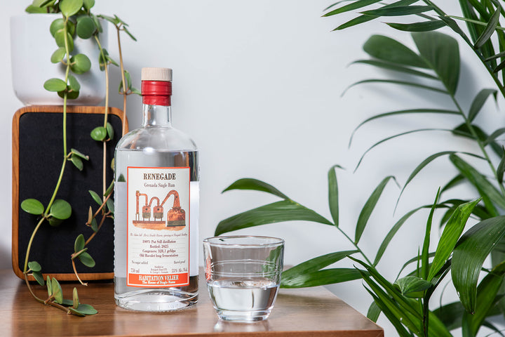 Renegade Rum bottle with a glass of water on a wooden surface with plants in the background