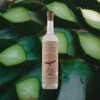 A tall thin bottle of mezcal with a craft paper label that reads: La Puritita Verda from Pierde Almas.  There's an illustration of a winged devil like creature diving into an agave plant. Set against a macro shot of freshly chopped agave pina, deep green in color.