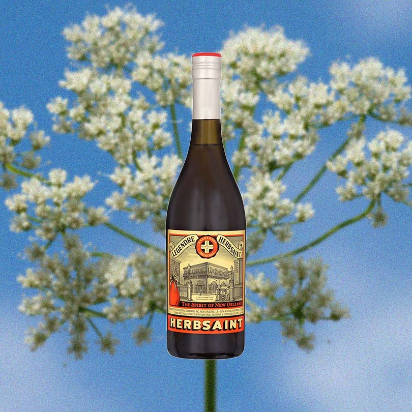 Bottle of Legendre Herbsaint Original Liqueur over backdrop of blue sky and flower.