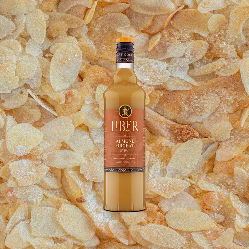 A bottle of Liber & Co. Almond Orgeat Syrup with a label showcasing the brand and product name, set against a background of sliced almonds.