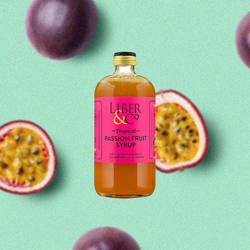 A large bottle of rich looking orange syrup with a fuschia label that reads: Liber & Co Tropical Passion Fruit Syrup. Set against a stylized back drop of passion fruits, and a light teal background.