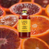 Bottle of Liber & Co. Blood Orange Cordial over backdrop image of halved oranges.