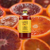 Bottle of Liber & Co. Blood Orange Cordial over backdrop image of halved oranges.