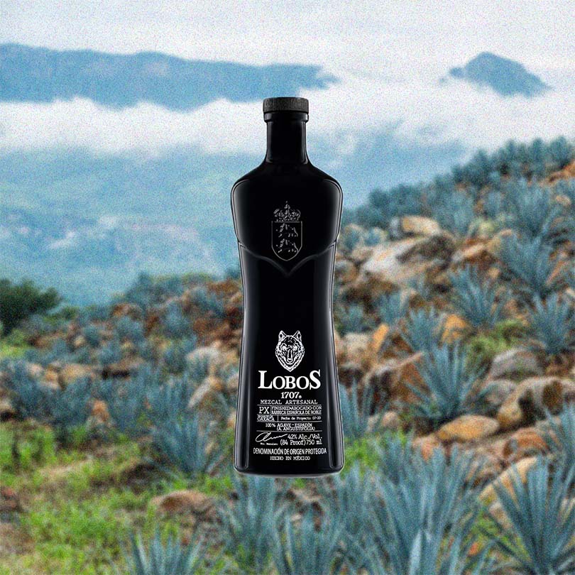 Bottle of Lobos 1707 Mezcal Artesanal over backdrop of blue agabve on a mountain side.
