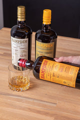 Hampden rum bottles being poured into a glass on a wooden surface.