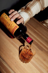 Person pouring a drink from a bottle labeled 'Hampden' into a glass on a wooden surface.