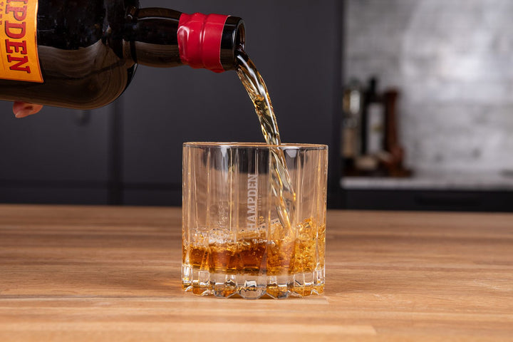 Amber-colored liquid being poured from a bottle into a glass on a wooden surface.