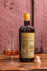 Bottle of Hampden rum with a glass on a wooden surface against a textured pink wall.