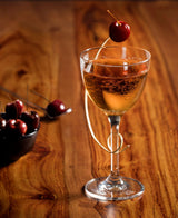 Glass of amber liquid with a cherry on a wooden surface