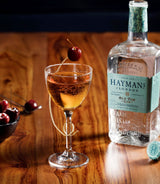 Hayman's gin bottle with a cocktail garnished with a cherry on a wooden surface