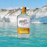 Bottle of Mater Sicilian Sugarcane Rum Yellow Cane Batch 1 over backdrop image of blue water coastline with cliffs.