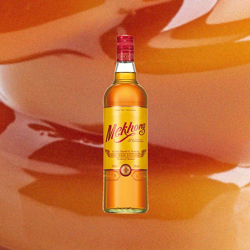 A large caramel colored bottle of liquid with a red screwtop cap. The label says: Mekhong The Spirit of Thailand.  This is set against a backdrop of rich browns, yellows, and butterscotch swirls, evoking the flavors of the spirit.
