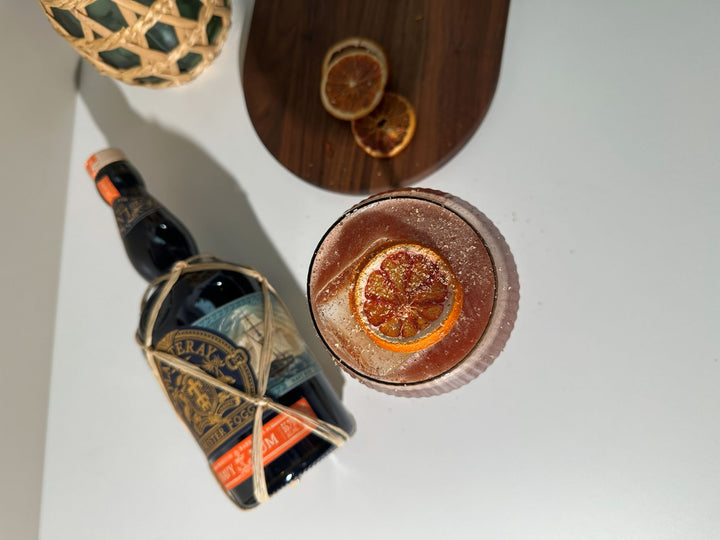 Cocktail with an orange slice and a bottle on a white surface