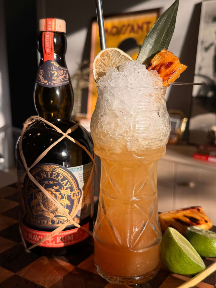 Bottle of Mister Fogg Rum next to a cocktail with lime and orange garnish on a checkered surface.