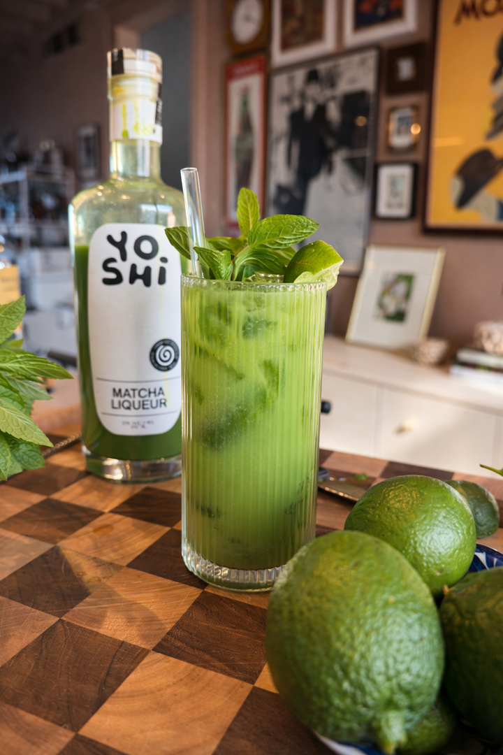 Green cocktail with mint leaves and a bottle of Yoshi Matcha Liqueur on a checkered table.