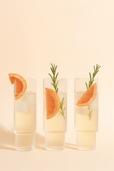 Three glasses of a citrus-themed drink with grapefruit slices and rosemary on a beige background
