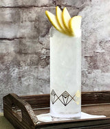 Cocktail in a decorative glass with lemon slices on a wooden tray against a stone wall.