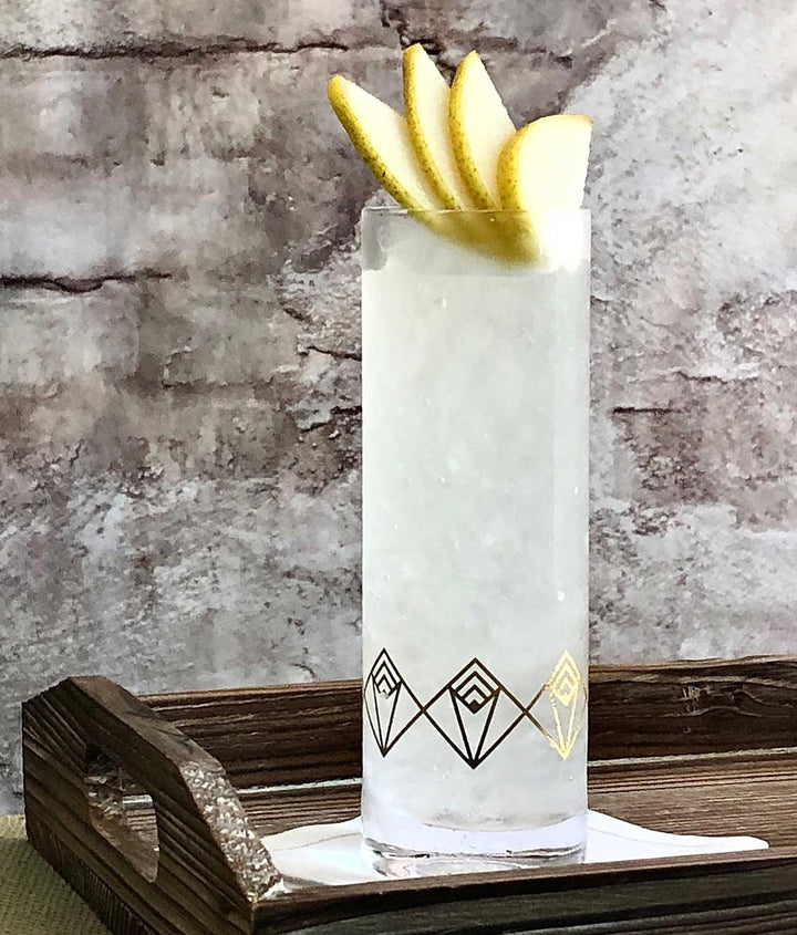 Cocktail in a decorative glass with lemon slices on a wooden tray against a stone wall.