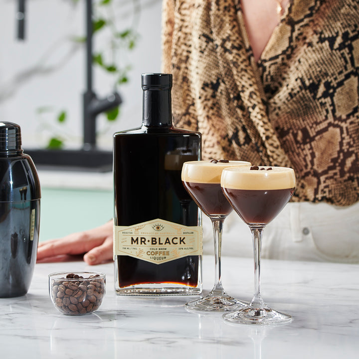 Bottle of Mr. Black coffee liqueur with two cocktails on a marble surface.