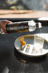 Bottle of Estrella Gin being poured into a glass on a dark surface with a blurred background