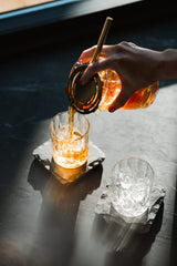 Hand pouring a drink from a bottle into a glass on a dark surface